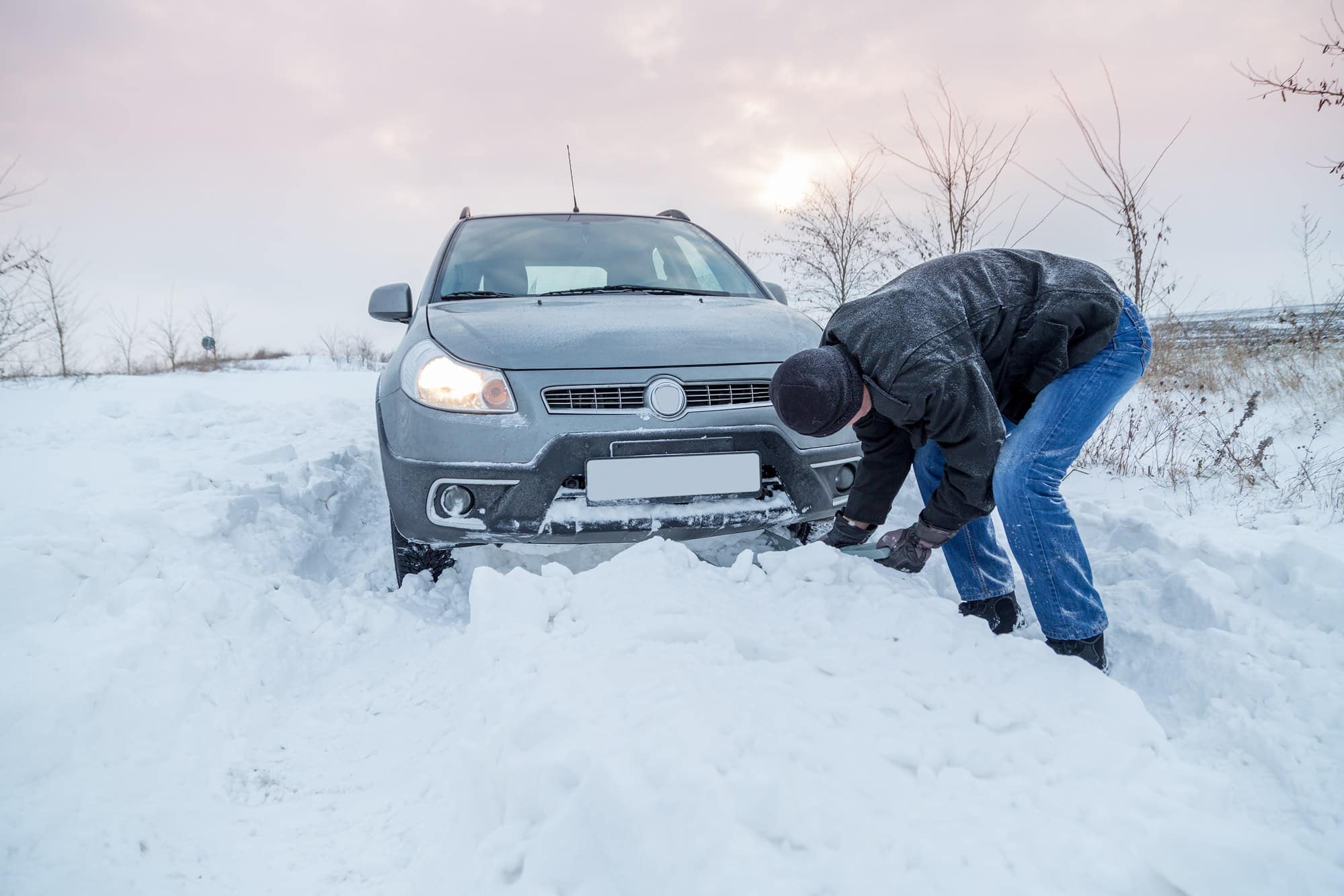 Man shoveling snow to free a stuck SUV during a winter recovery
