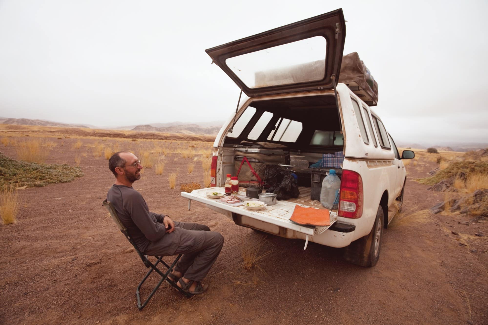 4x4 pickup camp at a desert campsite Man in a camp chair beside a 4x4 pickup with its canopy open and camp gear at a desert campsite