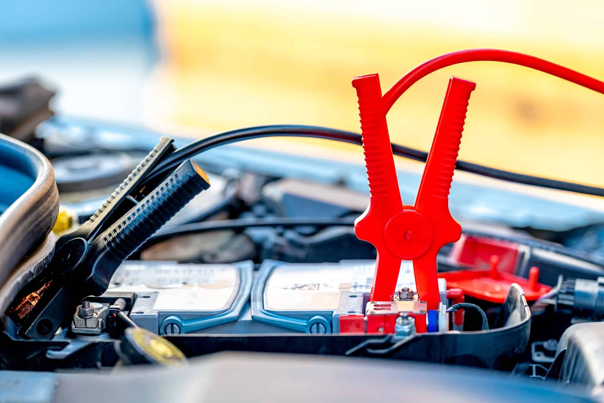 Red and black jump clamps connected to a car battery under the hood