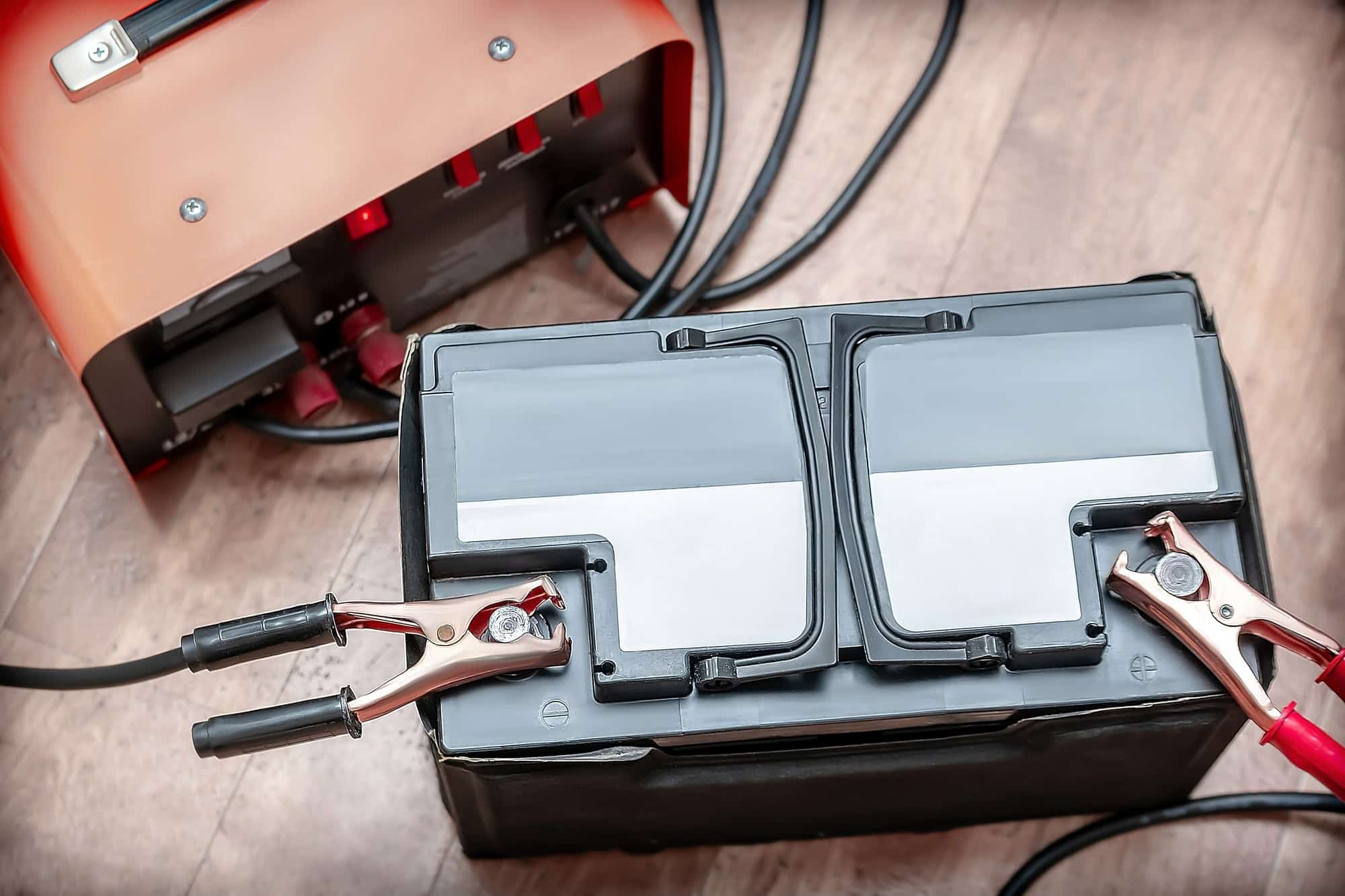 Battery charger clamps connected to a car battery on a garage floor