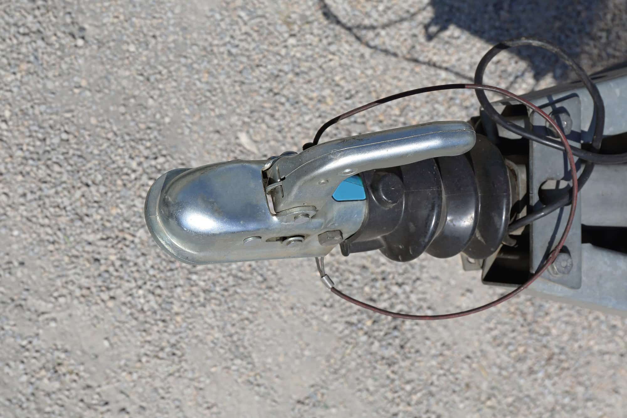 Trailer coupler and safety cable Top view of a trailer coupler with safety cable and wiring over gravel
