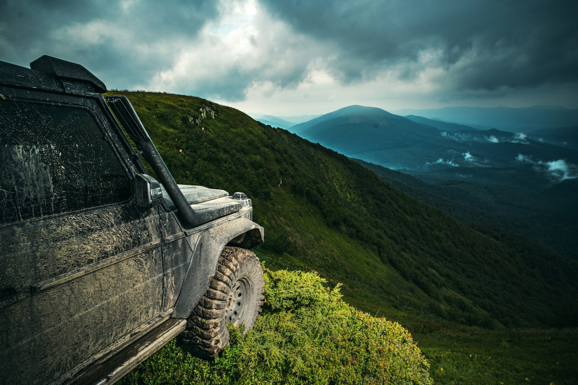 4x4 on a steep mountain slope Mud-covered 4x4 on a steep grassy mountain slope under storm clouds