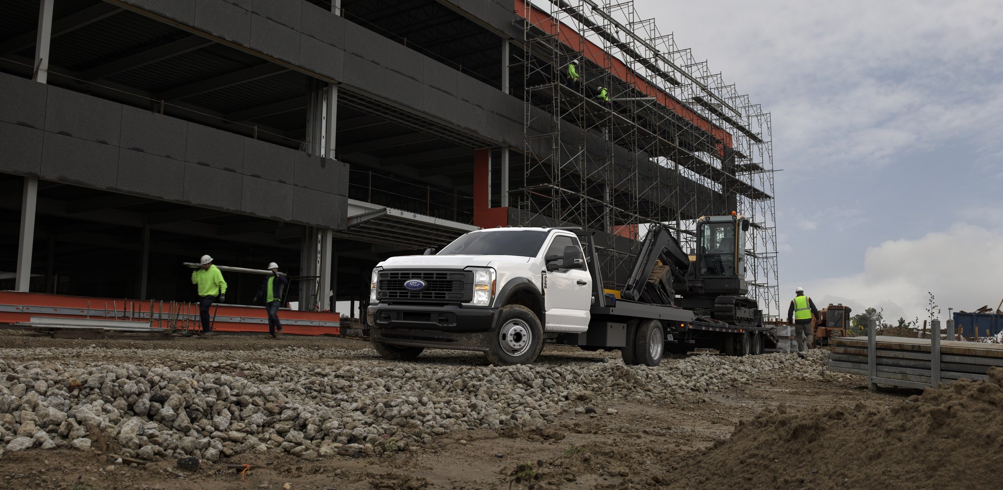 2025 Ford Super Duty chassis cab flatbed hauling a compact excavator at a construction site