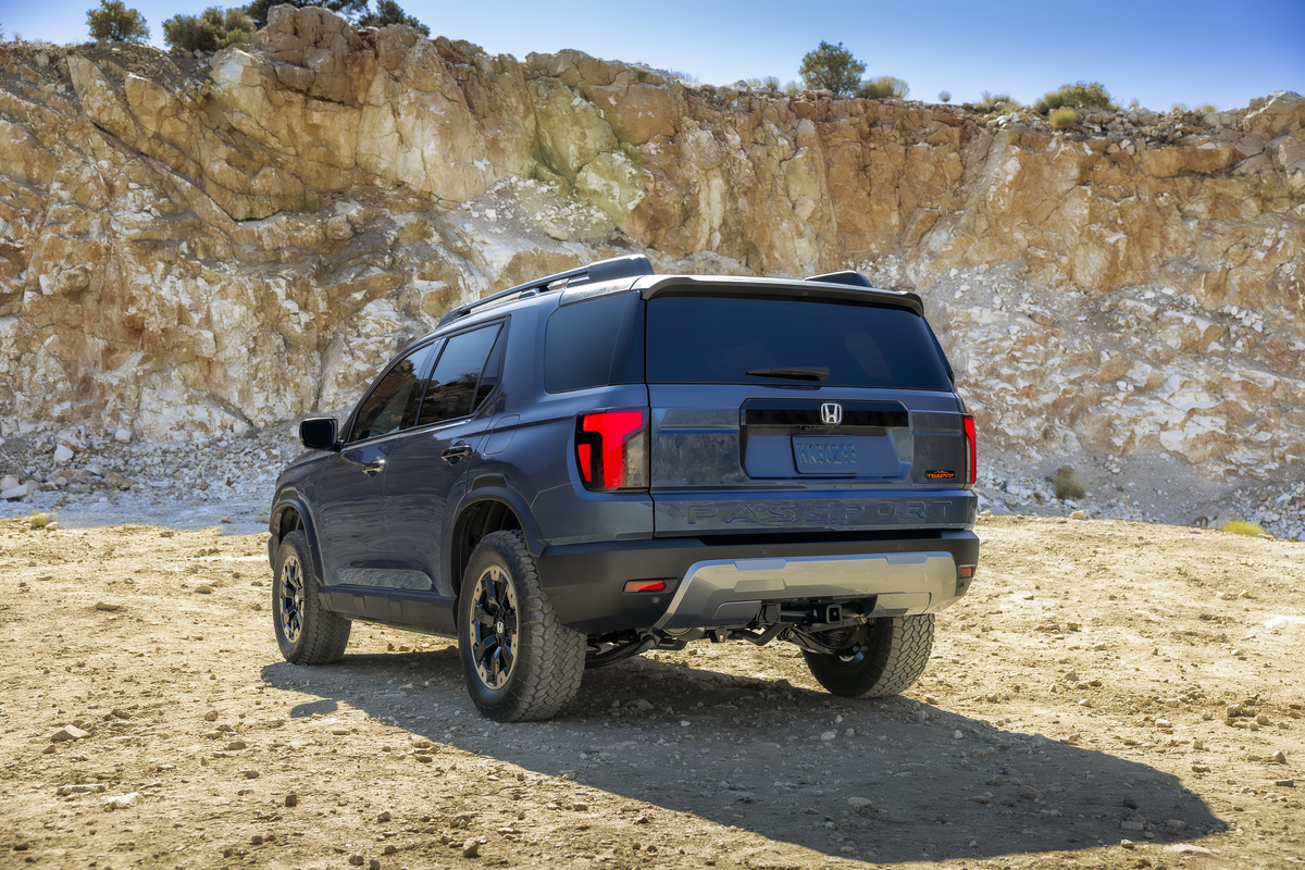 Rear view of a blue 2027 Honda Passport TrailSport parked on sand below a rock cliff