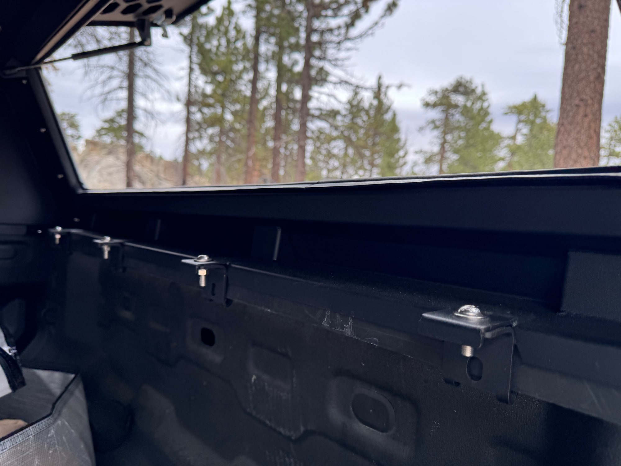 OPENROAD Truck Cap Bed-Rail Mounting Clamps Four mounting clamps along the inside bed rail beneath an open OPENROAD truck cap side door.