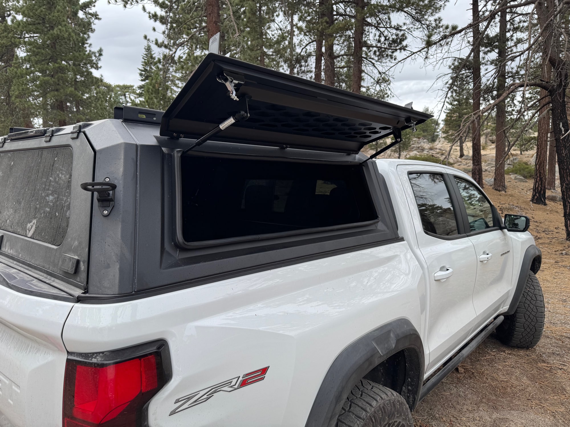 OPENROAD Truck Cap Side Door Open OPENROAD truck cap side door raised on support struts above the passenger side of a white Colorado ZR2.