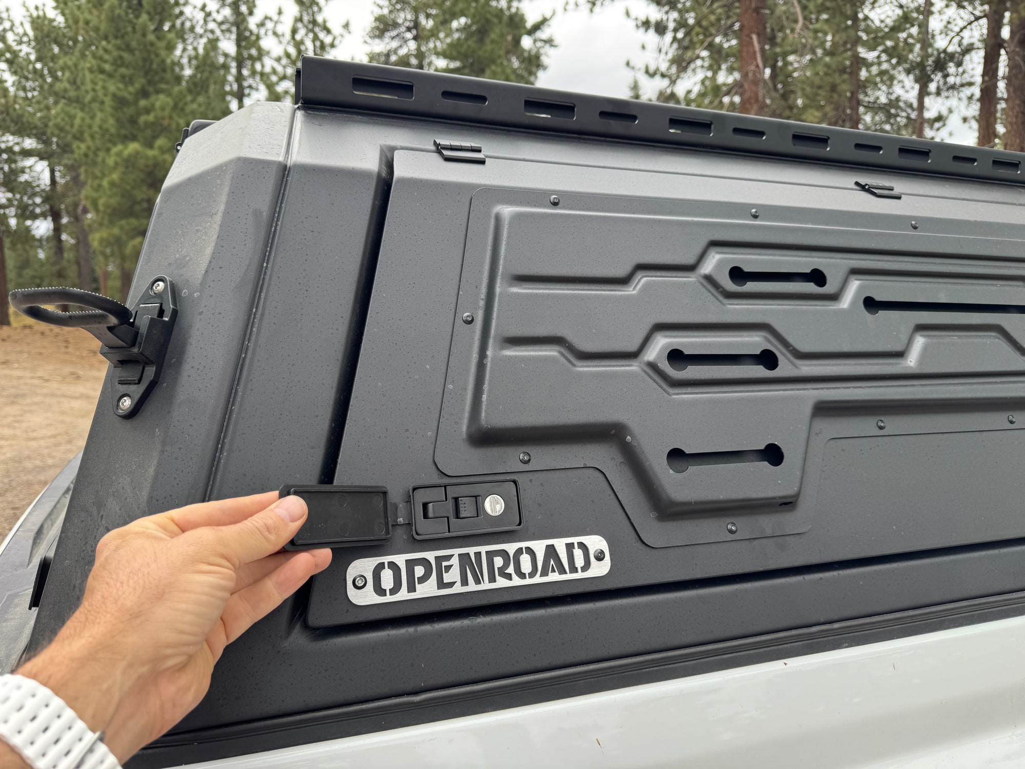 OPENROAD Truck Cap Lock and Rubber Cover Hand holding open the rubber cover over an OPENROAD truck cap side-door latch and key lock.