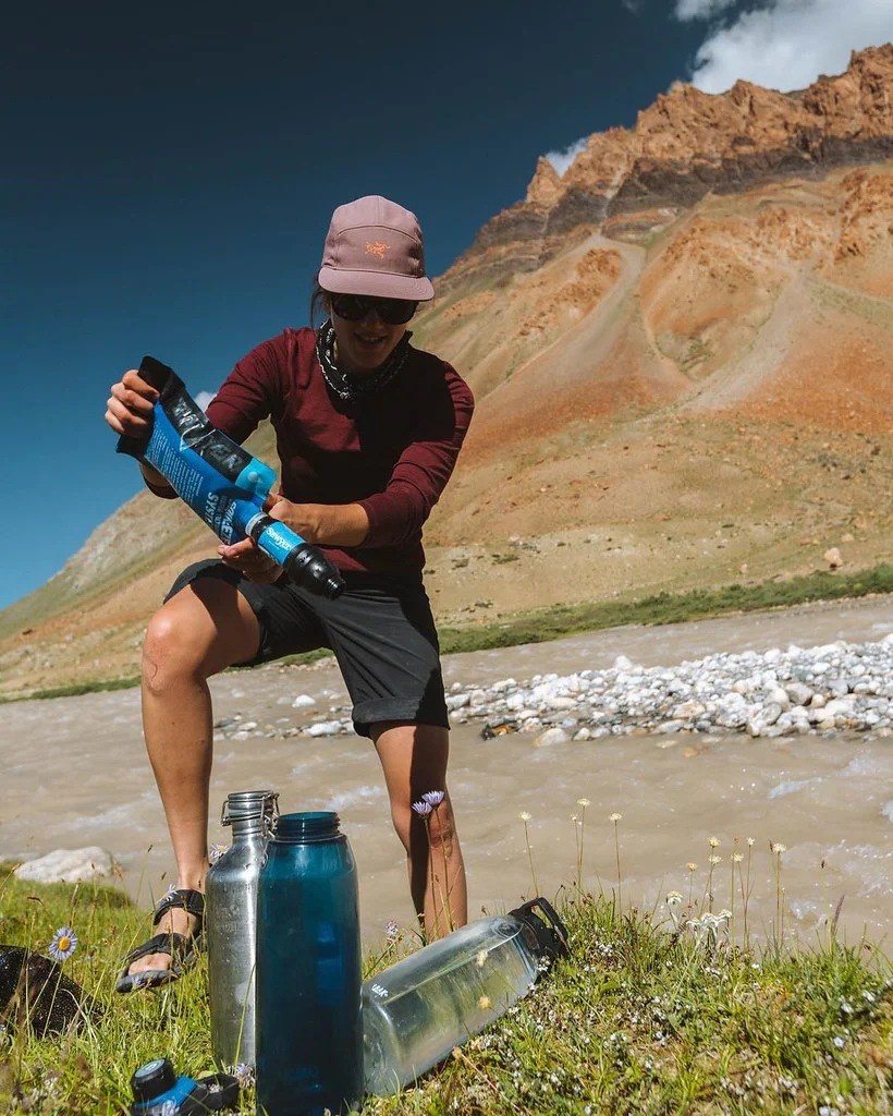 Sawyer Squeeze water filter in use Sawyer Squeeze water filter pouch in use by a hiker in front of mountains