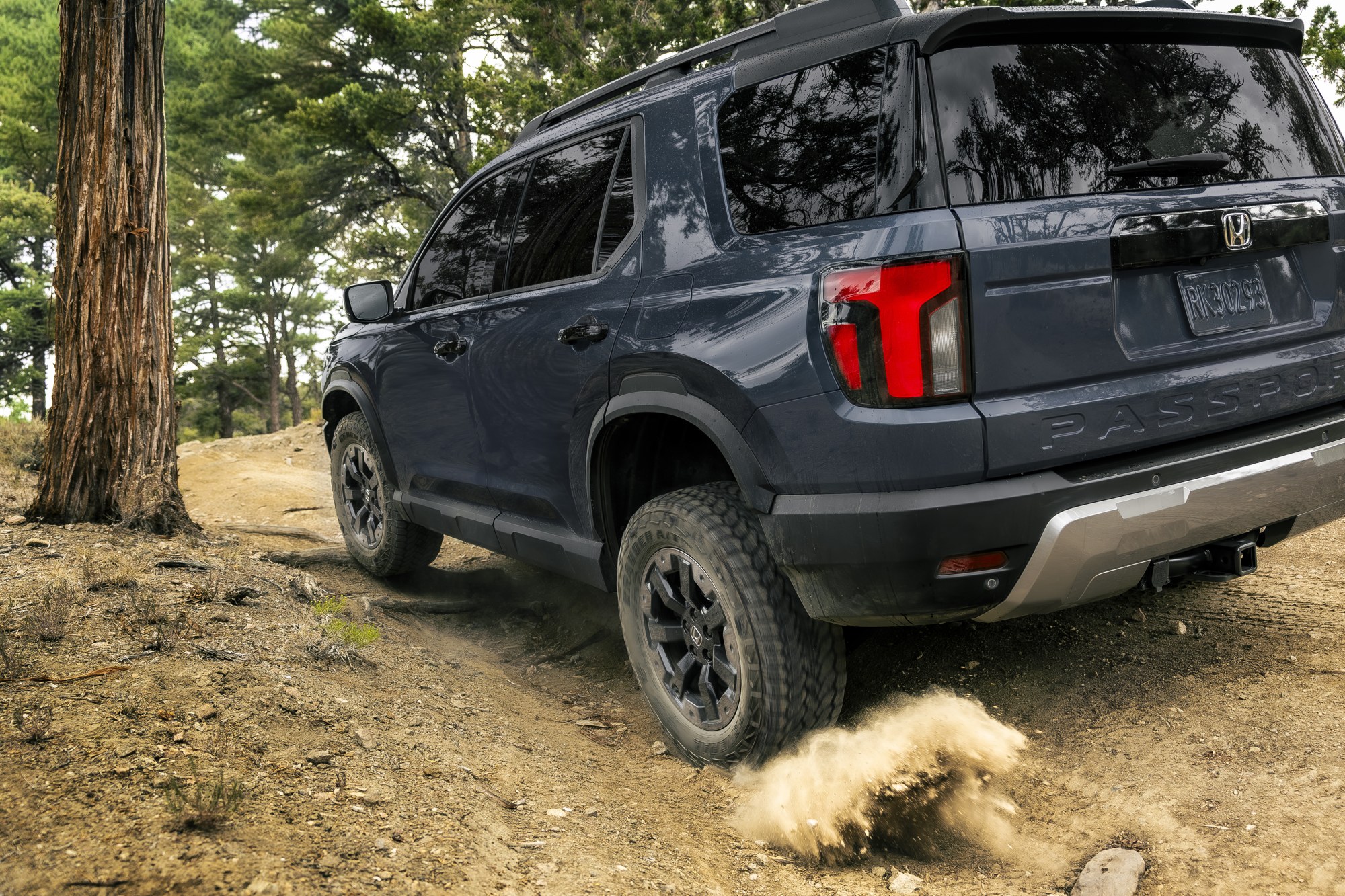 2027 Honda Passport TrailSport kicking up dust on a dirt trail among pine trees