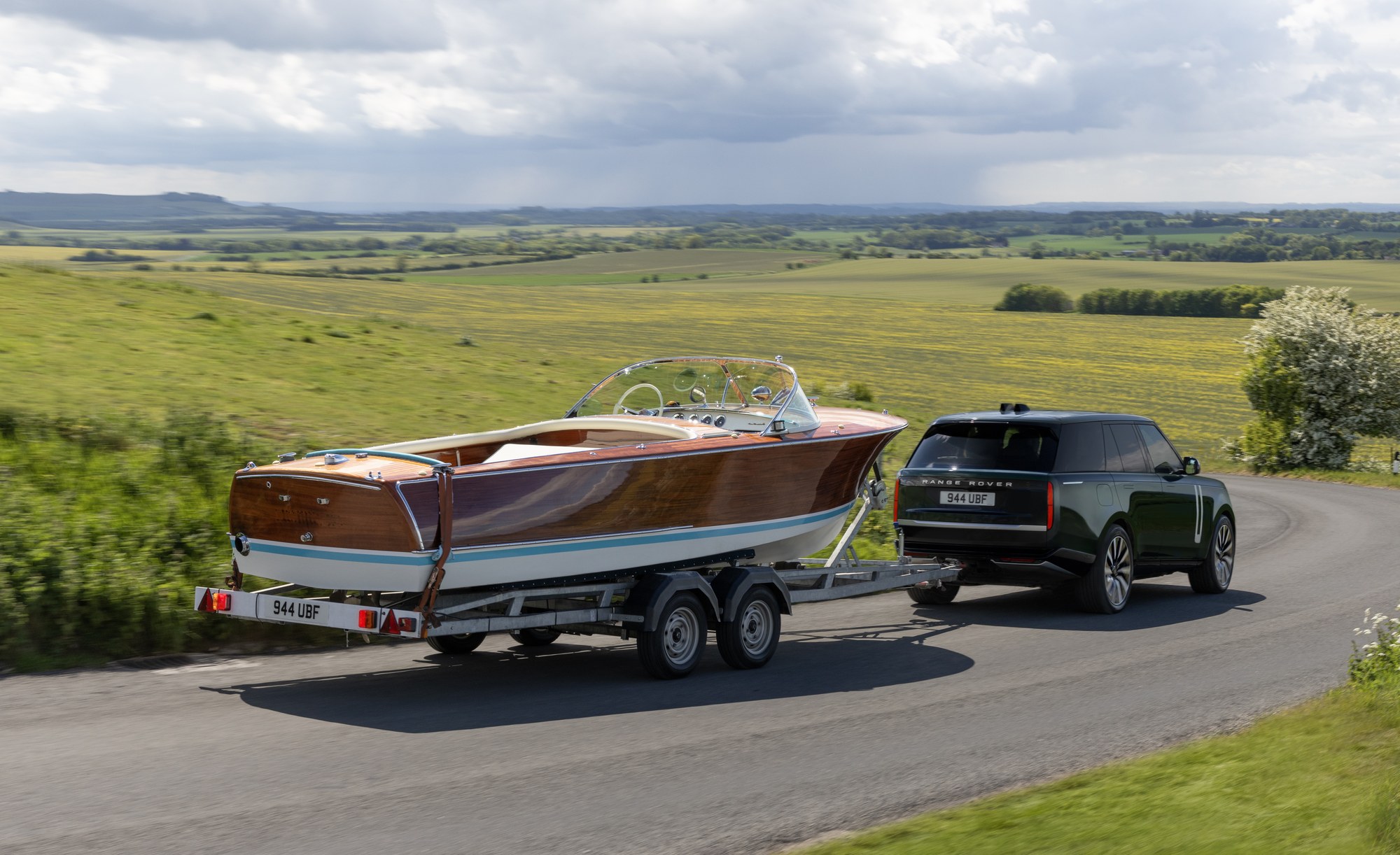 Electric Range Rover towing a wooden speedboat on a trailer along a country road
