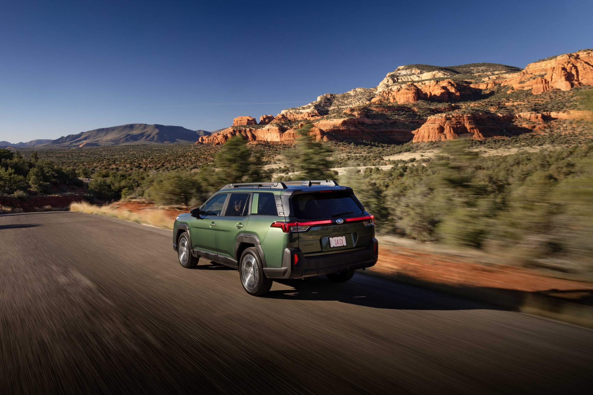 Green Subaru Outback driving on a desert road past red rock cliffs