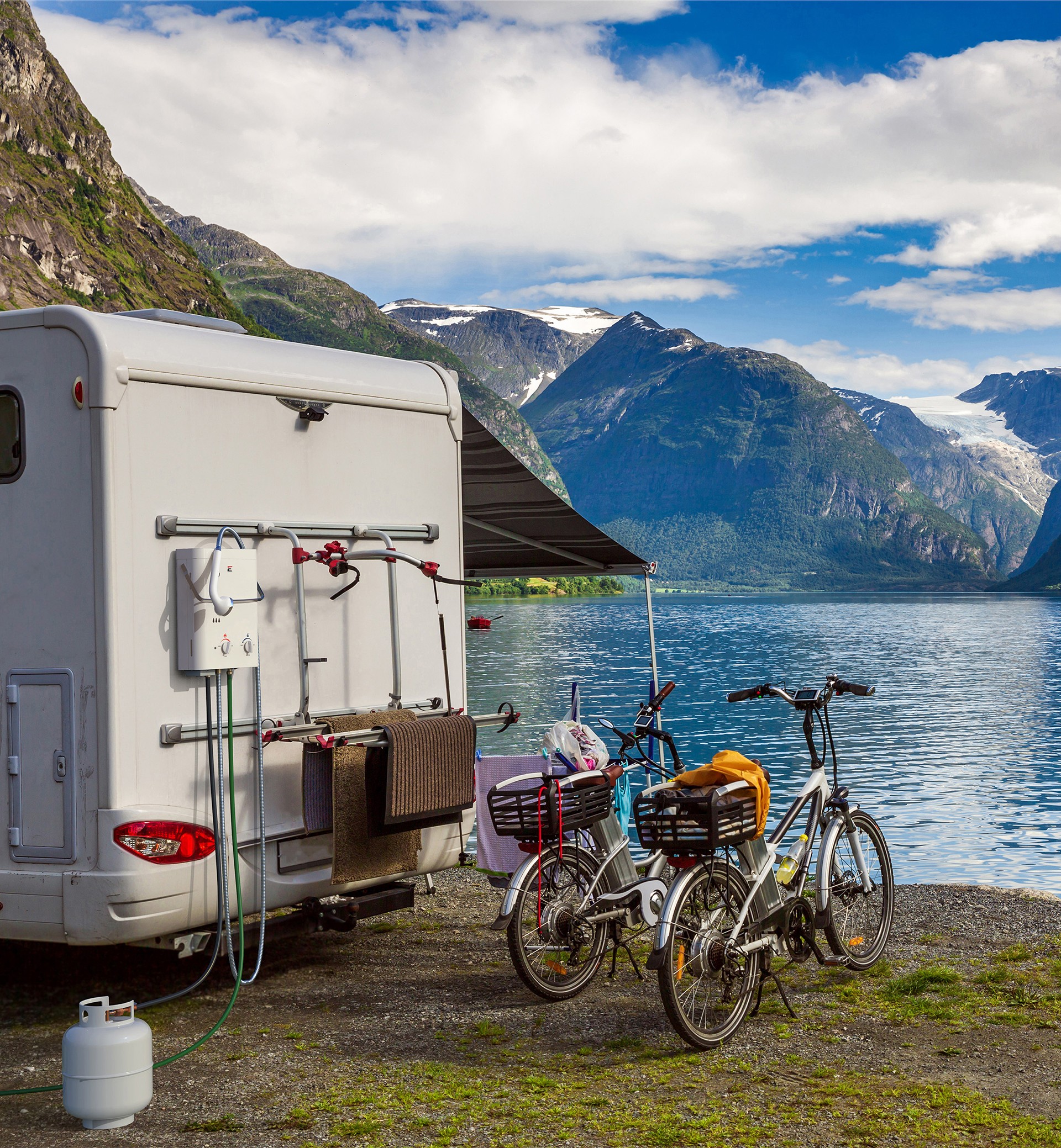 Eccotemp L5 portable water heater mounted on the side of a camper at a lakeside camp with a propane tank below