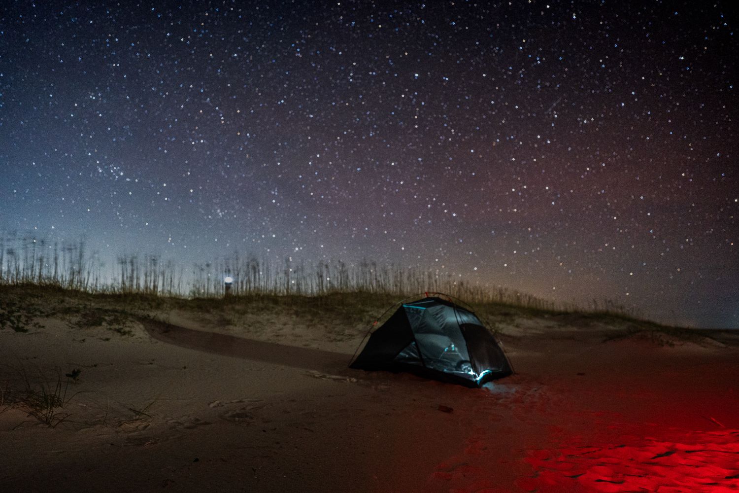 Tent camping under the stars at Cape Lookout Camper using a red light beside a tent on the dunes under a starry sky at Cape Lookout National Seashore
