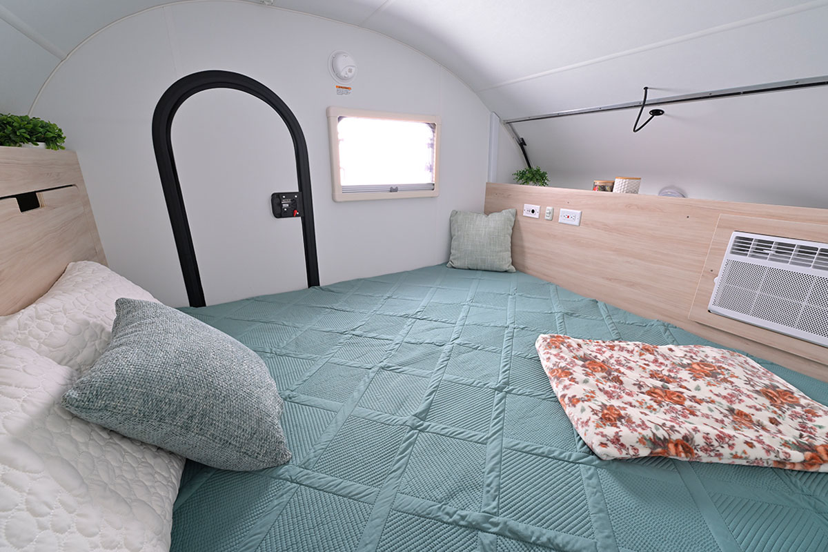 Bed with a quilted blue cover inside the nuCamp teardrop cabin