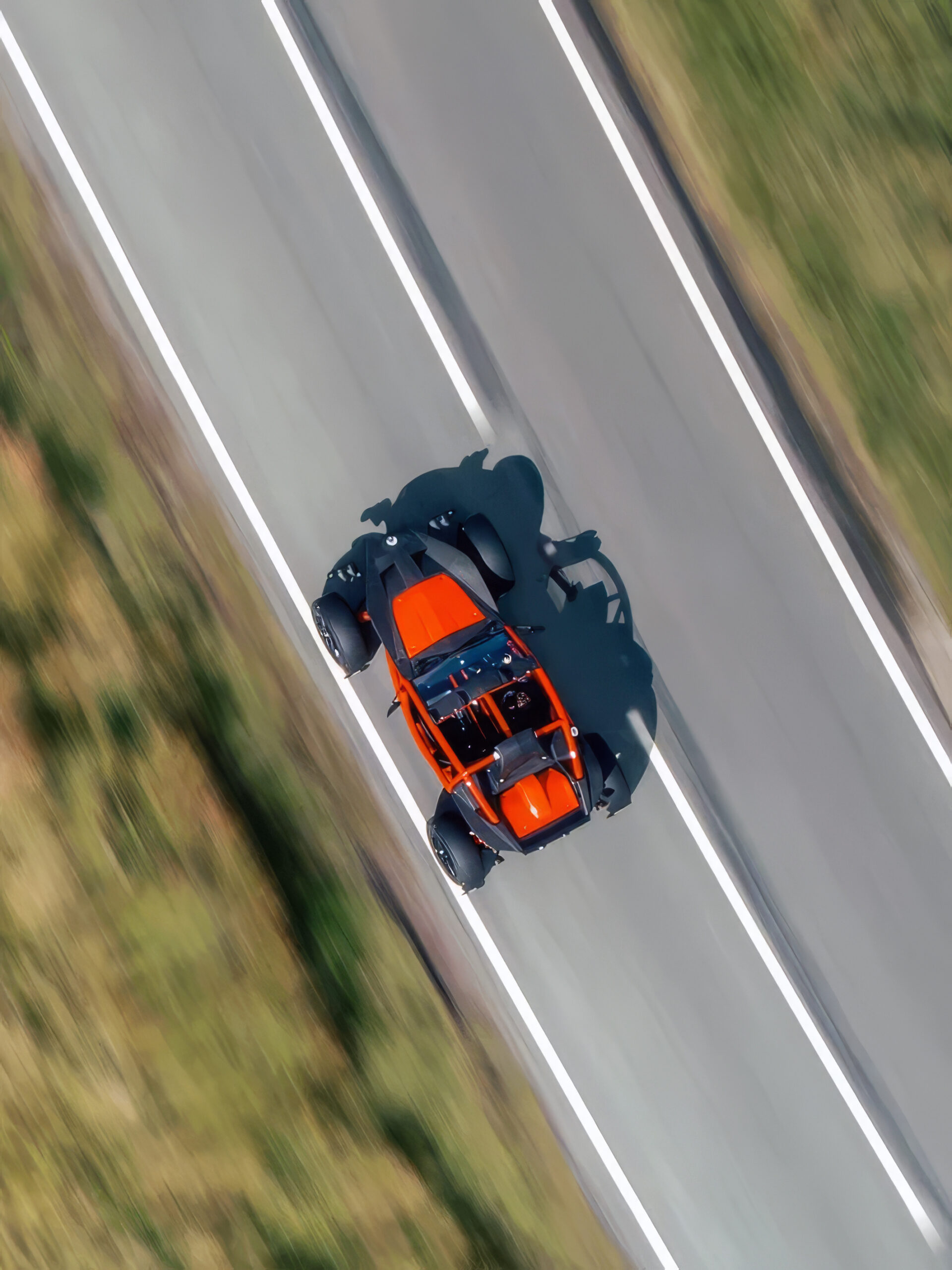 Overhead drone view of an orange Ariel Nomad 2 driving a two-lane road
