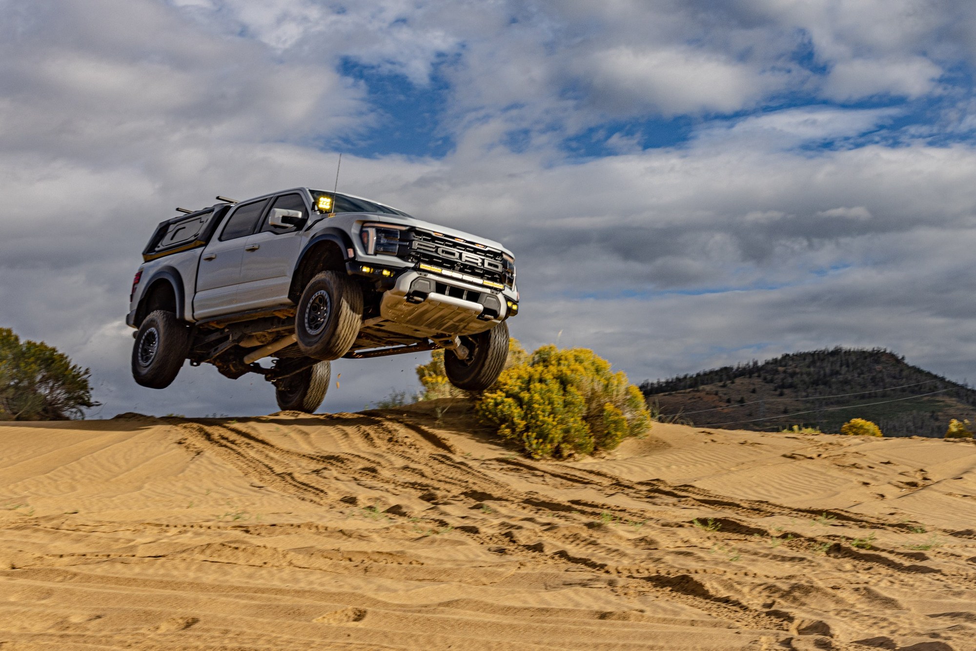 Ford F-150 Raptor with a Narwhal carbon fiber topper airborne over a sand dune